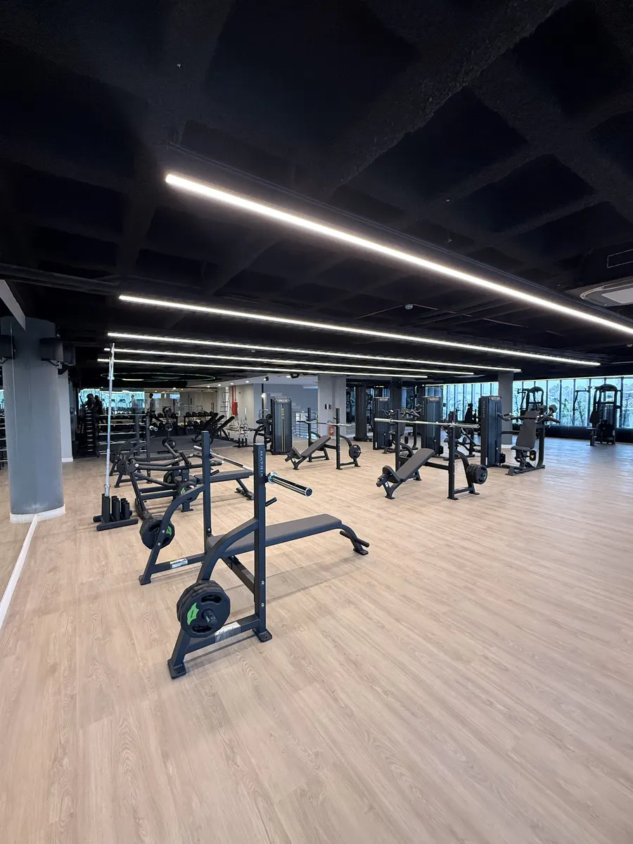Área de musculação com piso de madeira e iluminação em linha